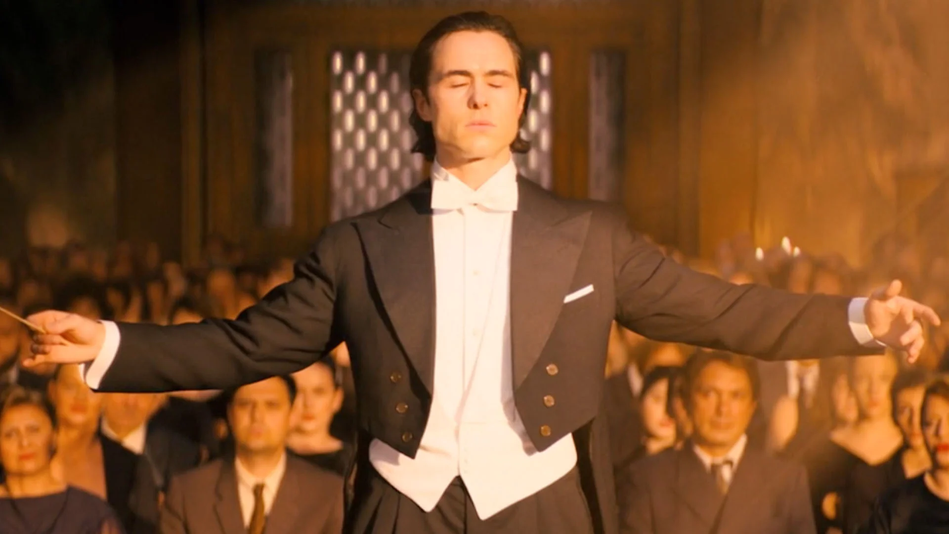 Conductor in a Black Tuxedo with White Bow Tie Conducts an Orchestra with Arms Spread Wide Eyes Closed