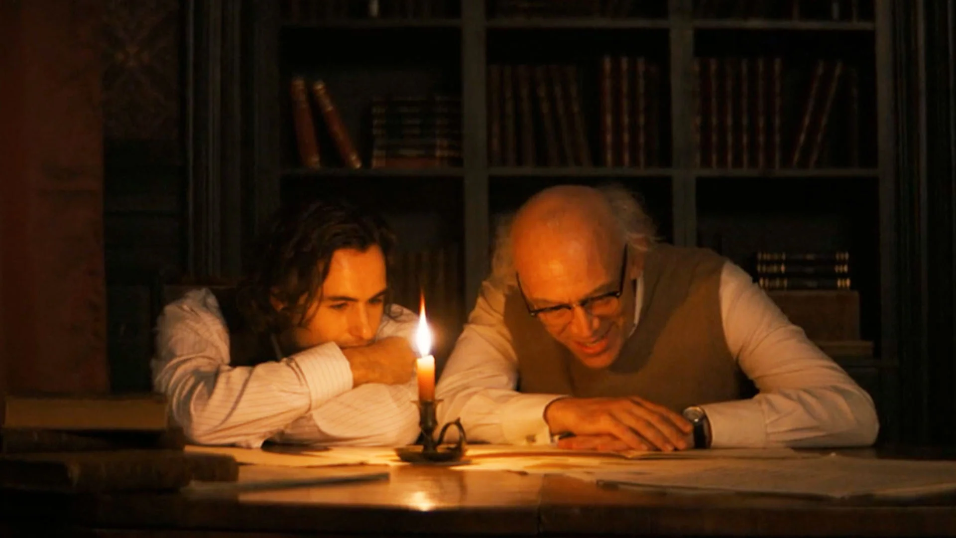 Two Men Sit at a Wooden Table by Candlelight Studying Together in a Dim Library Setting