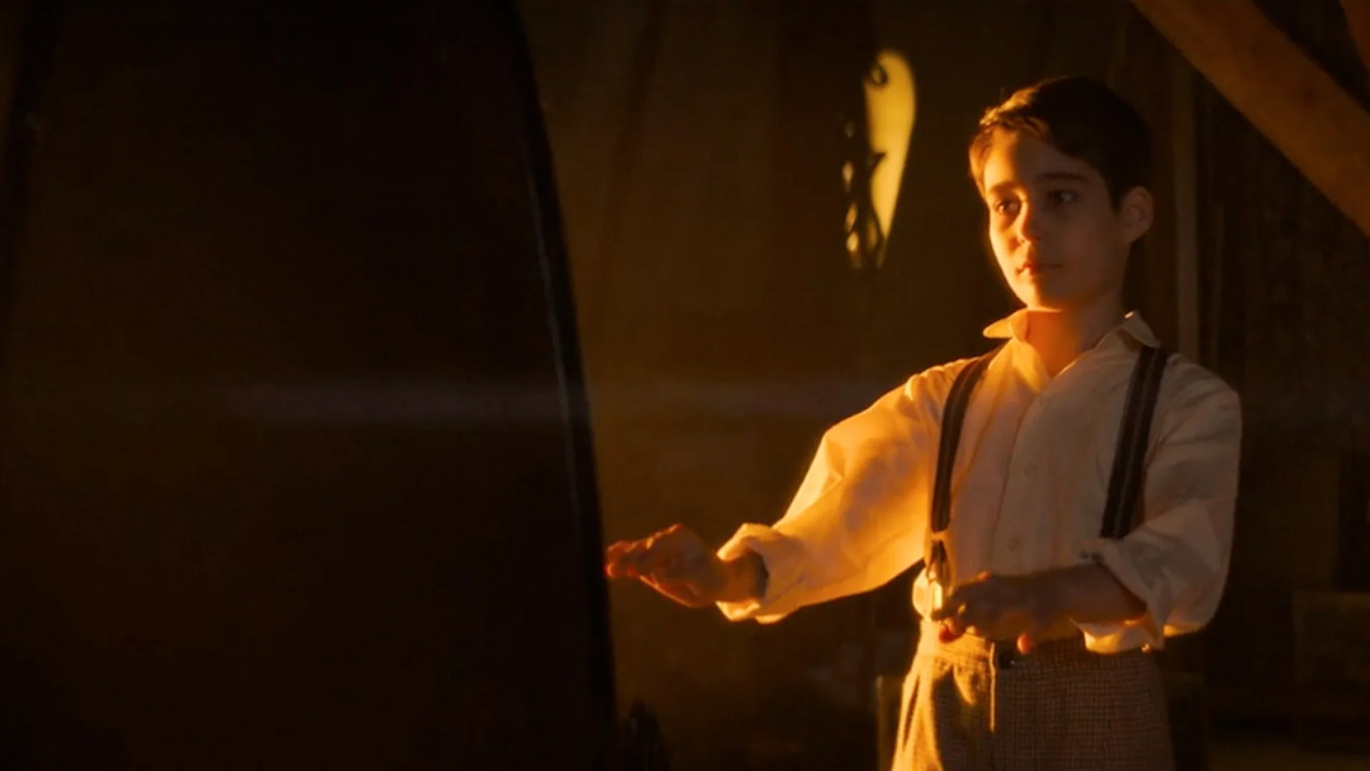 Young Boy in Old fashioned Shirt and Suspenders Stands by a Glowing Furnace Hands Outstretched Toward the Heat