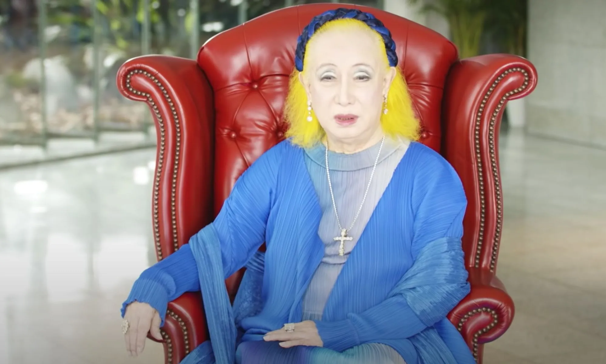 Older Woman with Bright Yellow Hair and Blue Outfit Sitting in a Red Tufted Leather Armchair