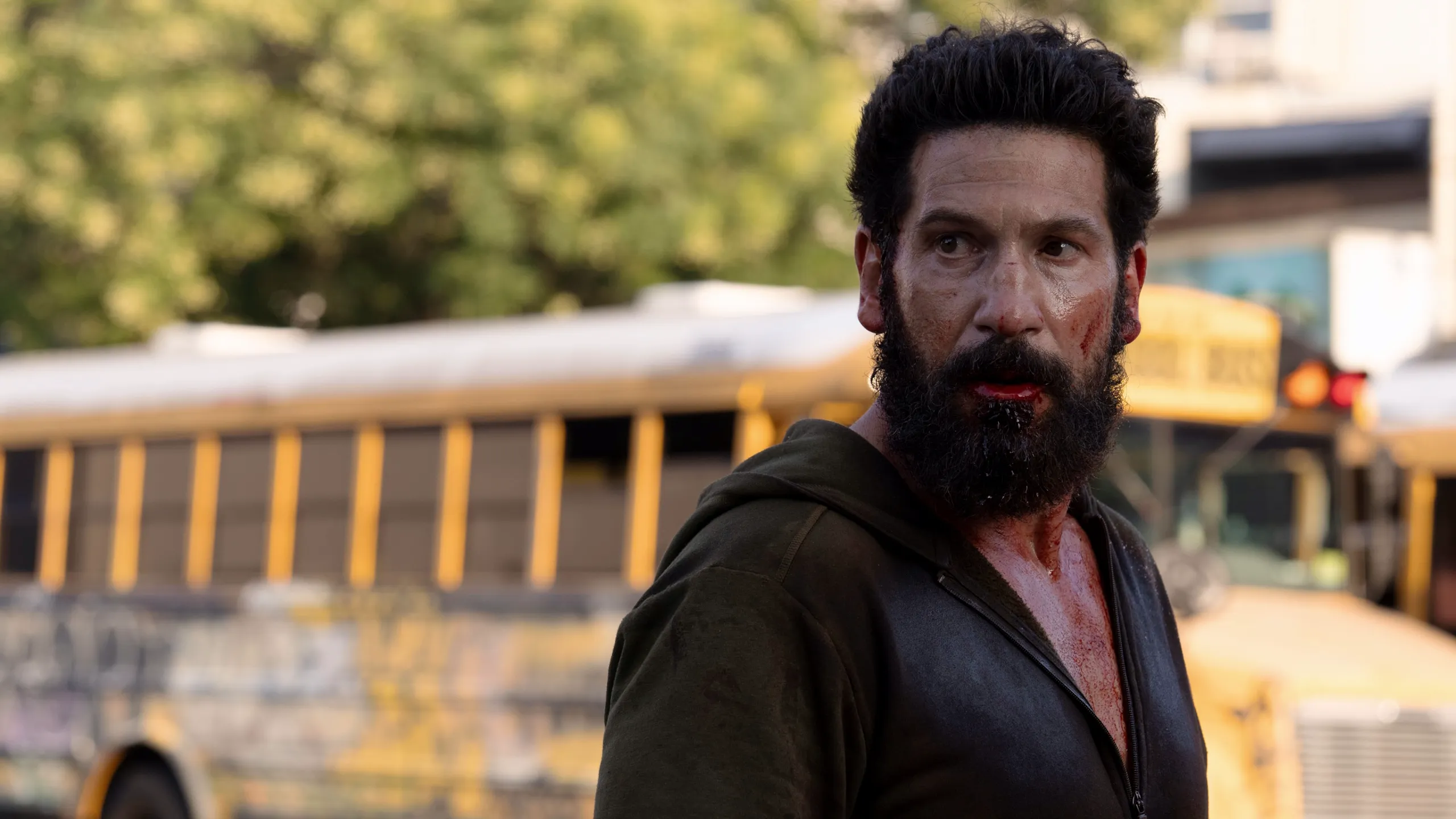 Bearded Man with Blood on His Face Looking to the Right Outdoors Beside a Yellow Bus in a Parking Lot