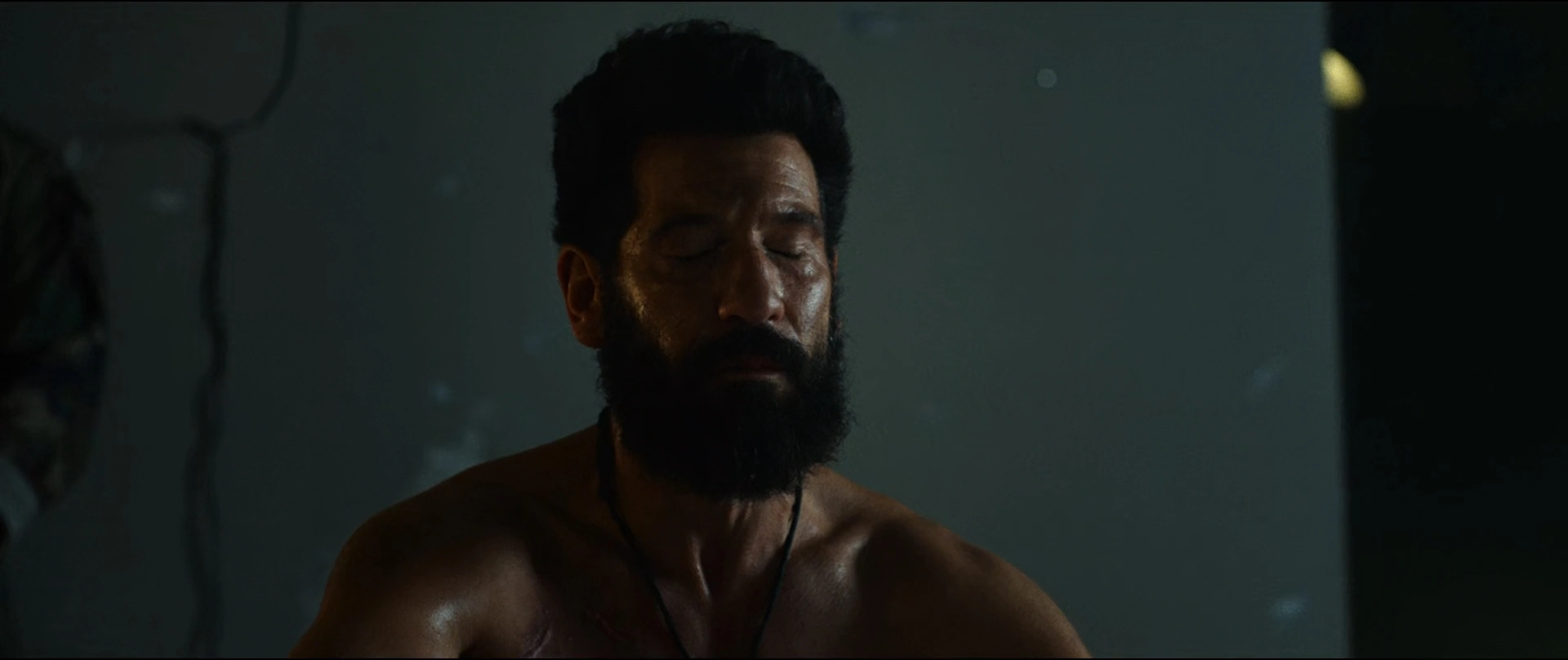 Man with Dark Beard and Closed Eyes Shirtless in a Dim Moody Room Possibly Meditating or Resting