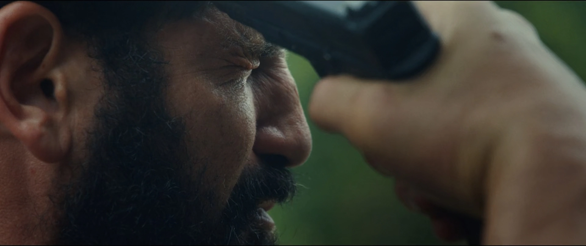 Close up of a Bearded Man Squinting As a Hand Holds a Black Device to His Eye likely Binoculars