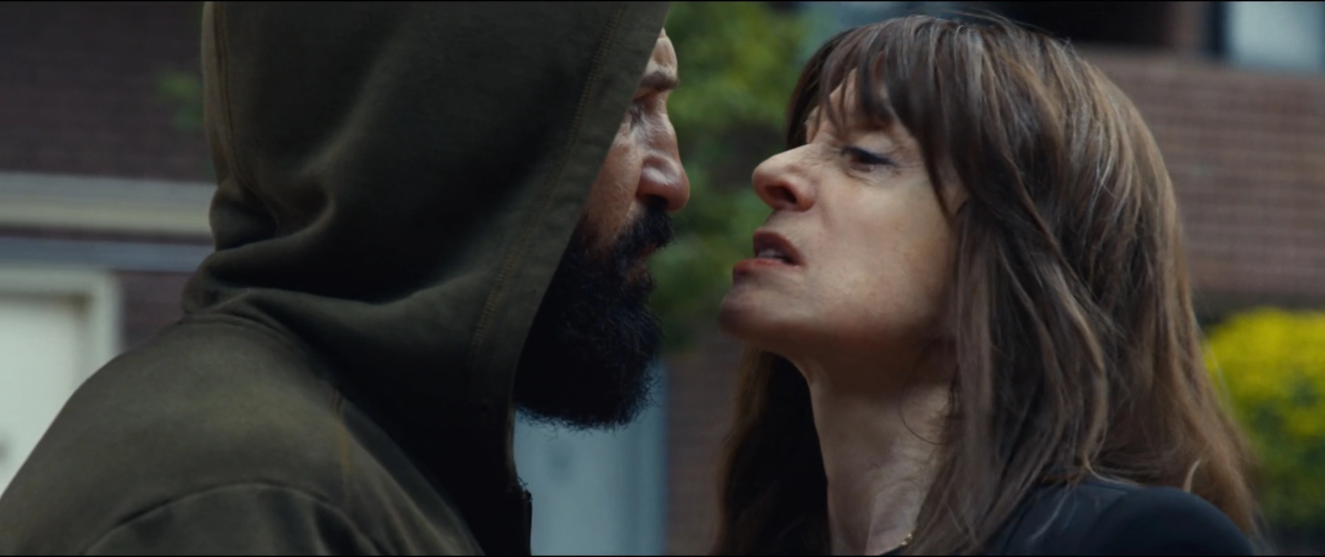 Close up of a Hooded Man with a Beard Leaning in Toward a Woman with Long Brown Hair on Outdoor Setting Tense Confrontation