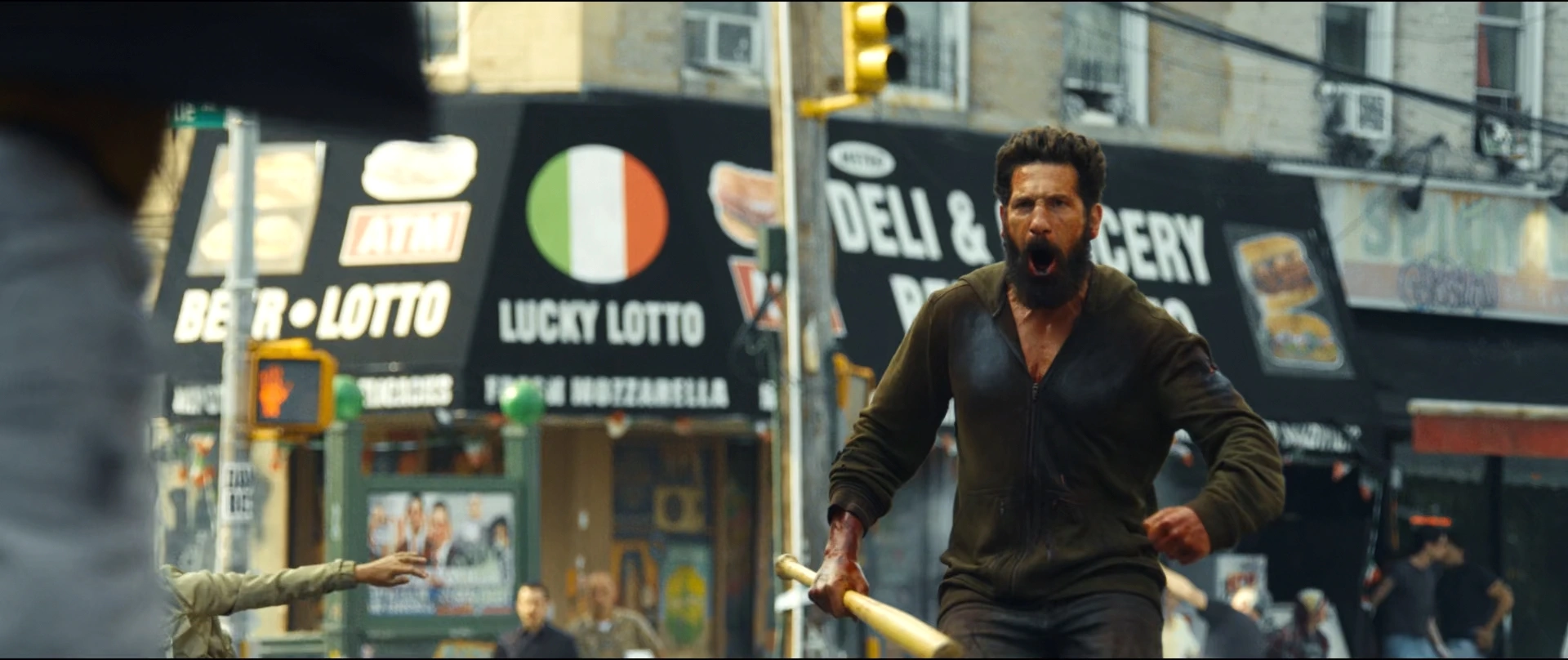 Bearded Man in a Brown Jacket Charges Forward with a Wooden Baton on a Busy City Street