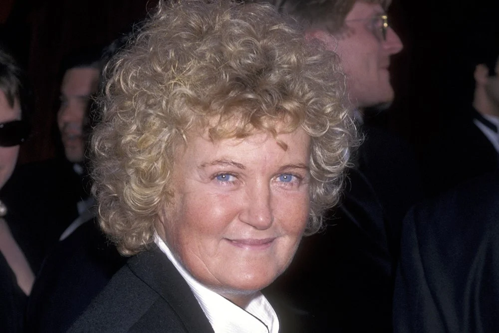 1000051382 Smiling Woman with Short Curly Blond Hair in a Dark Coat at a Formal Event