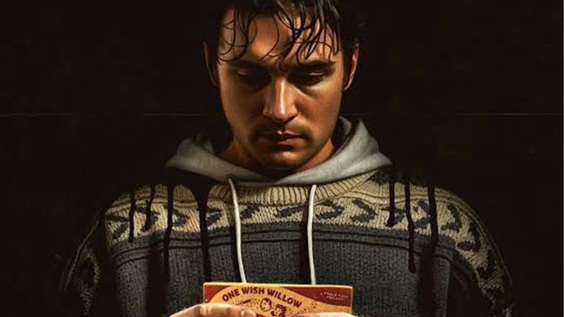 Man in a Patterned Gray Hoodie Reads a Small Orange Book in Low Lighting Looking Down
